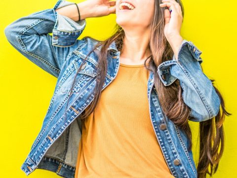 Smiling Woman Looking Upright Standing Against Yellow Wall