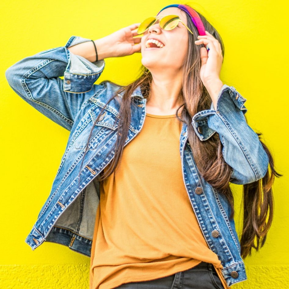 Smiling Woman Looking Upright Standing Against Yellow Wall